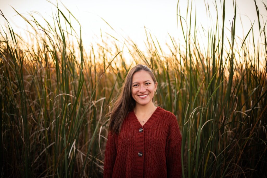 Woman in red cardigan standing among tall reeds at sunset