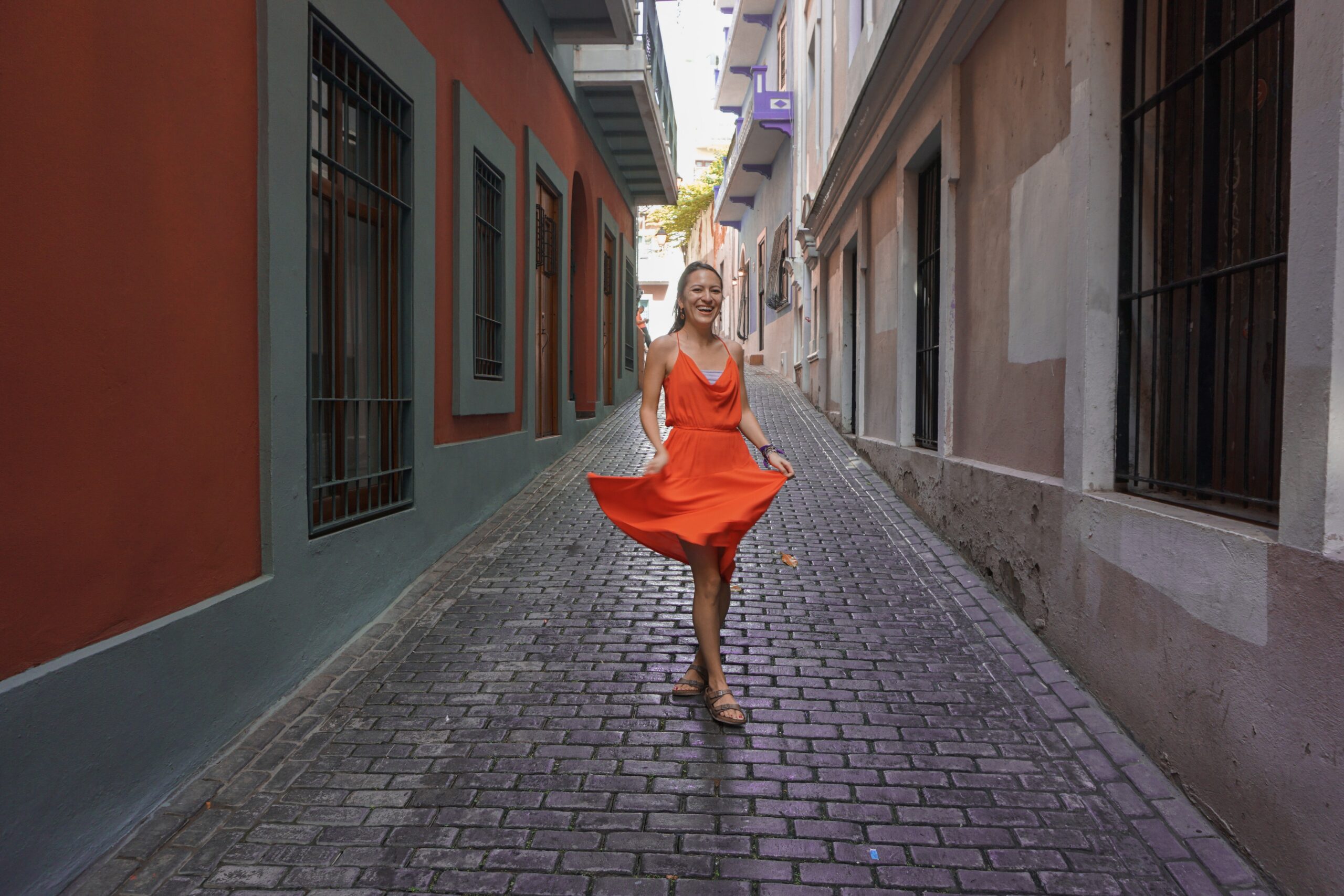 Woman in red orange dress twirling in narrow empty street in san juan puerto rico