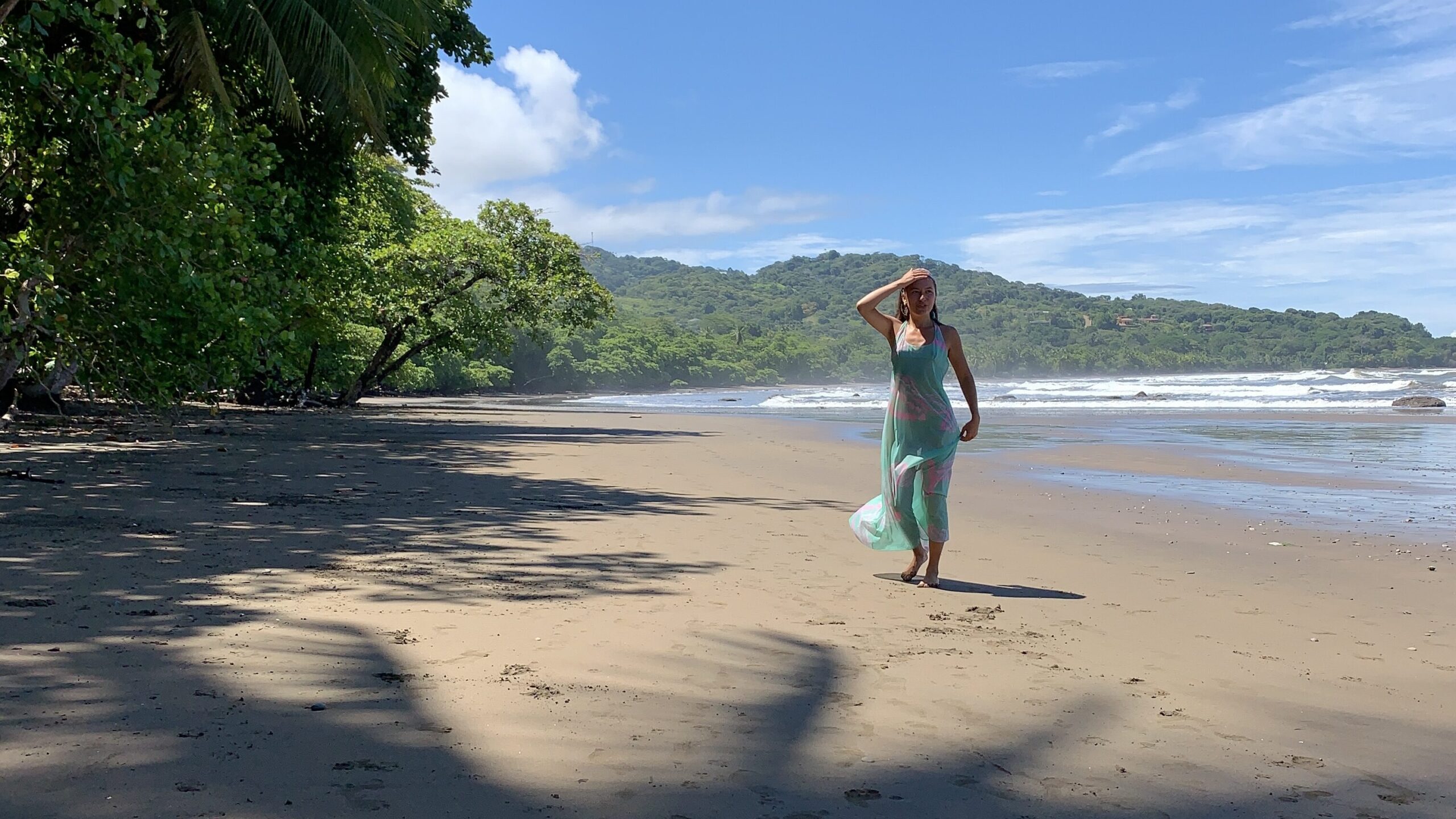 Woman in long dress at beach with ocean and palm trees around her