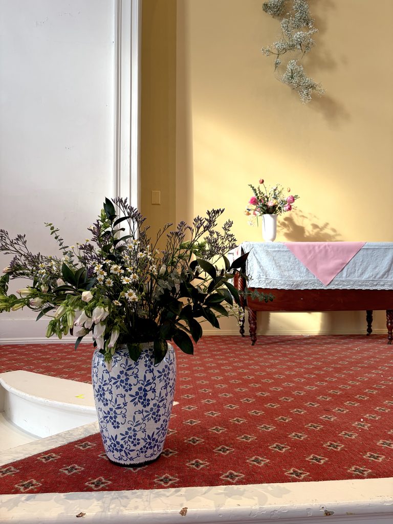 White and blue large vase with greenery, white flowers, bells of ireland, and heather florals.