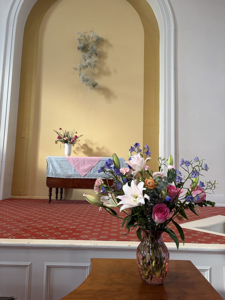 Front of church with two floral arrangements and a hanging art floral piece. Intentional floral design.