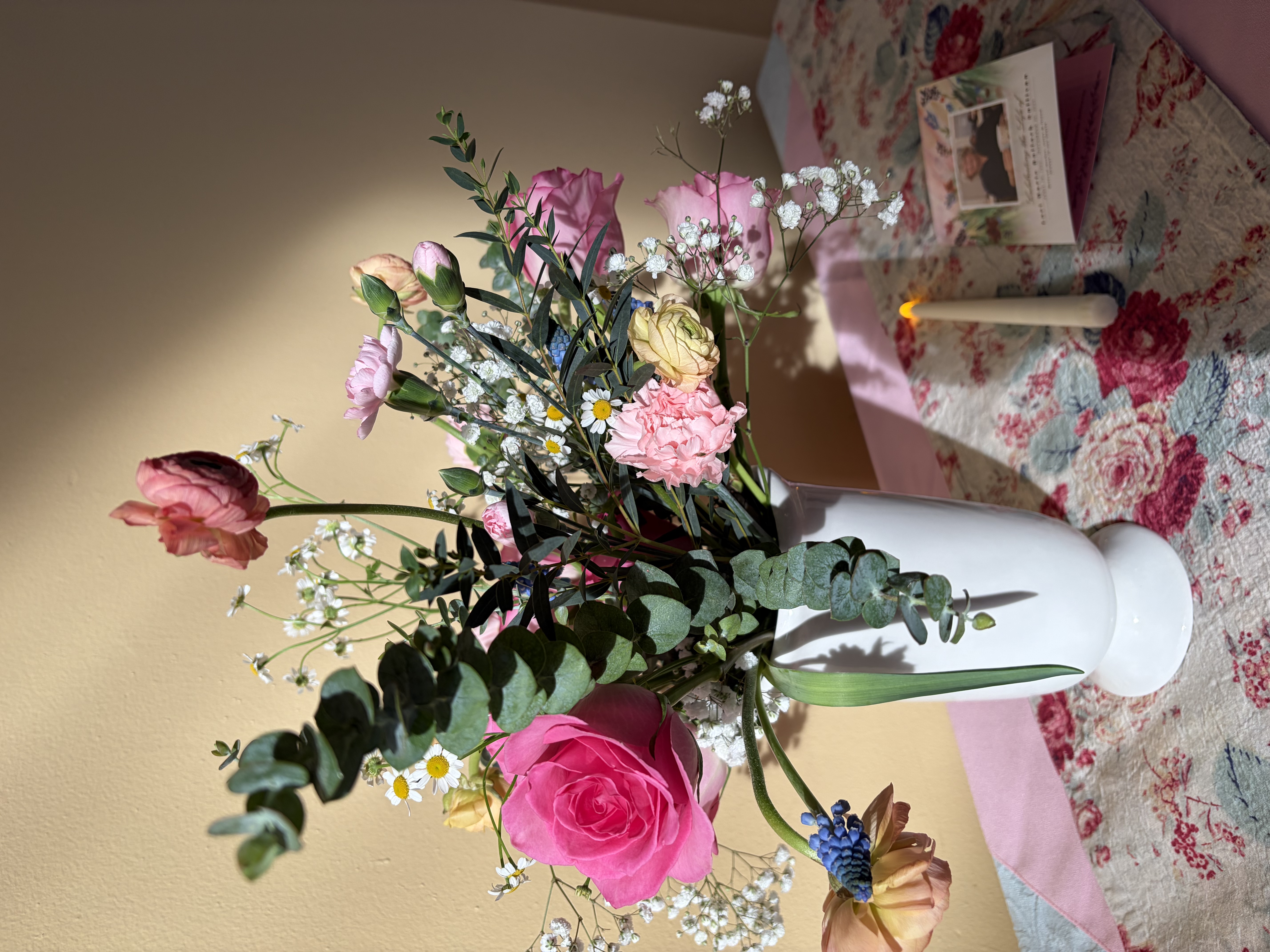 White tall vase with eucalyptus, pink roses, peach ranunculus, pink carnations, and accent flowers for celebration of life floral design arrangement.