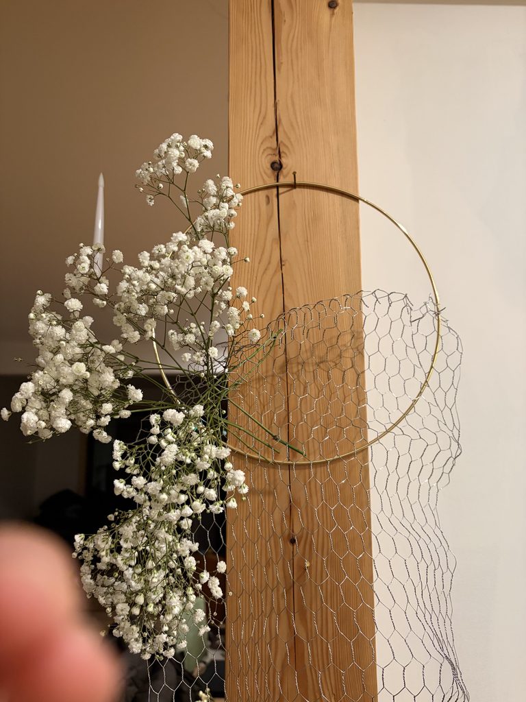 Gold hoop with silver chicken wire hanging down from it with baby's breath woven between.